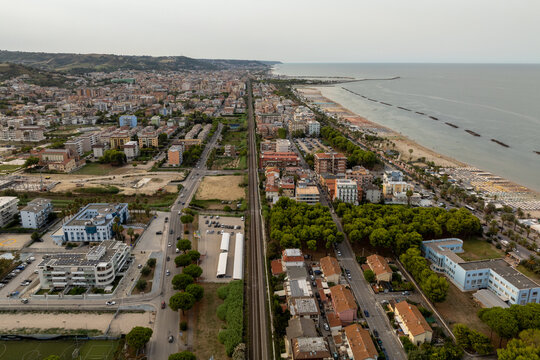 Aerial view of the railway line running parallel to the sandy beach, urban buildings, and green trees in San Benedetto del Tronto, Marche, Italy.