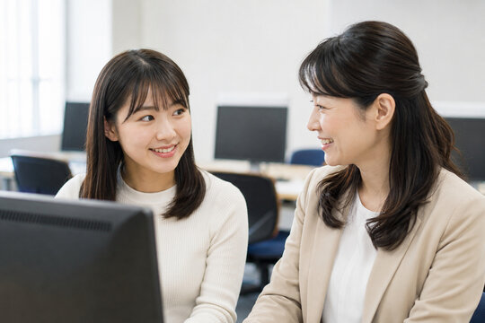 PC訓練の入力結果を笑顔で確認する日本人女性と支援員