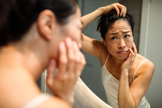 Concerned woman checking gray hair in bathroom mirror