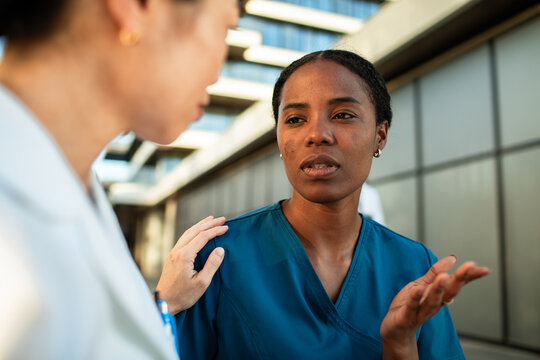 Concerned nurse comforted by colleague outside hospital