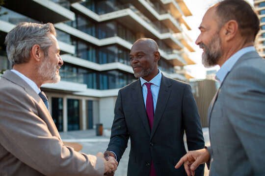 Three business executives shaking hands outside modern office building