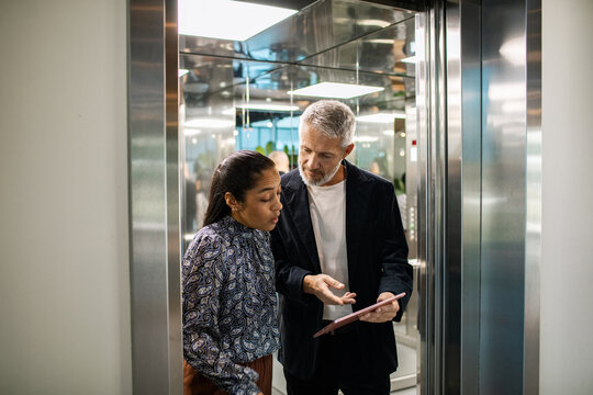 Two business colleagues discussing a tablet in an office elevator