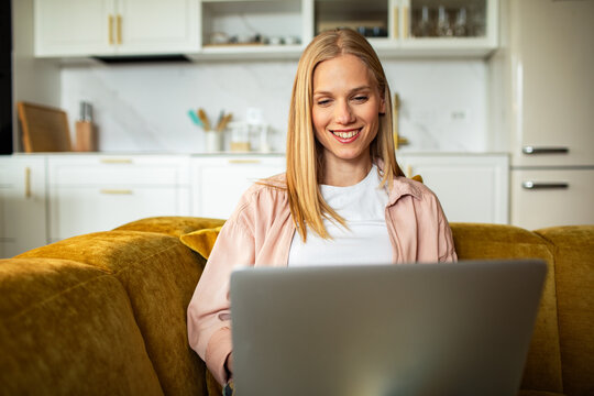 Smiling woman working on laptop on sofa at home