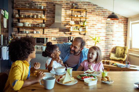 Father and three children laughing over breakfast in home kitchen