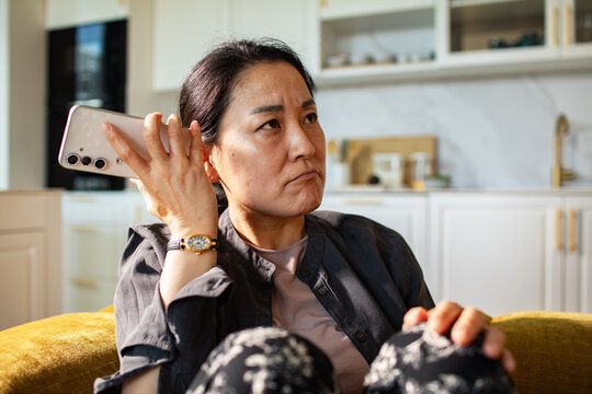 Frustrated woman holding smartphone during call in home kitchen