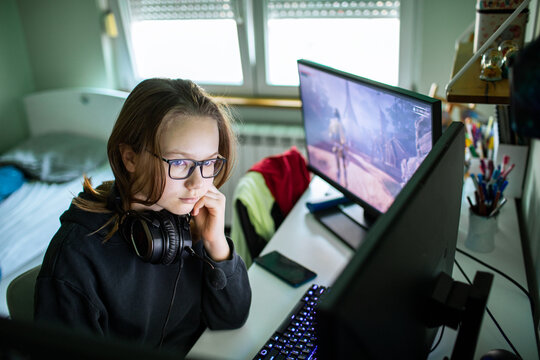 Teen girl gaming with headset at dual monitor pc in bedroom
