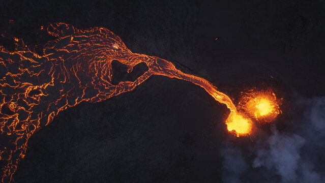 Aerial view of an active volcanic eruption with glowing molten lava flowing across a dark landscape in Reykjavik, Reykjavikurborg, Iceland.