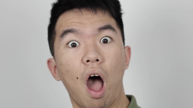 A young Asian man shows a surprised expression with wide eyes and an open mouth, for shock, reaction, unexpected news, or emotional response concepts.