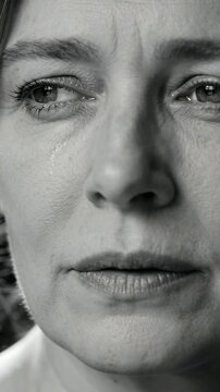 Vertical video: Exhaling midlife woman letting tear track down cheek in close-up, with collar, sad