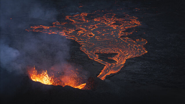 Aerial view of an active volcano erupting with glowing lava flows and volcanic smoke in the dark landscape of Reykjavik, Reykjavikurborg, Iceland.