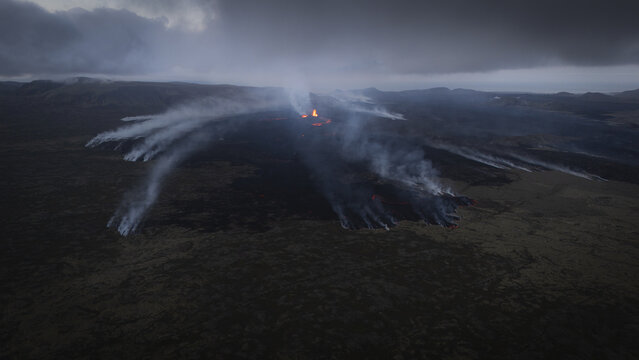 Aerial view of an active volcanic eruption with glowing lava and smoke plumes rising over the dark, rugged landscape of Reykjavik, Reykjavikurborg, Iceland.