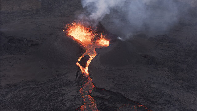 Aerial view of active volcano erupting with glowing lava flows and volcanic smoke rising from the crater in Reykjavik, Reykjavikurborg, Iceland.