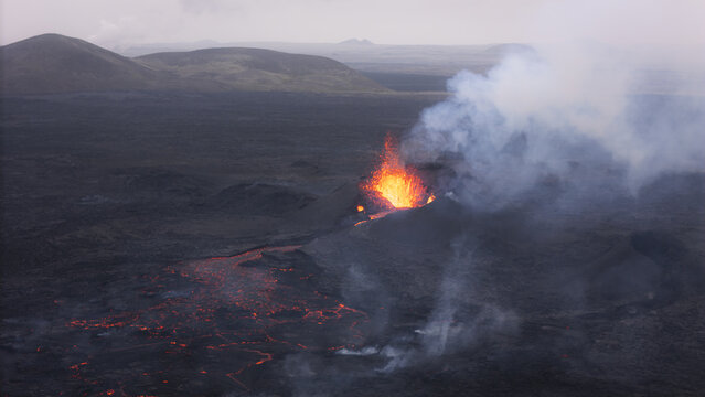 Aerial view of an active volcano erupting with glowing lava flows and volcanic smoke rising over the rugged landscape in Reykjavik, Reykjavikurborg, Iceland.
