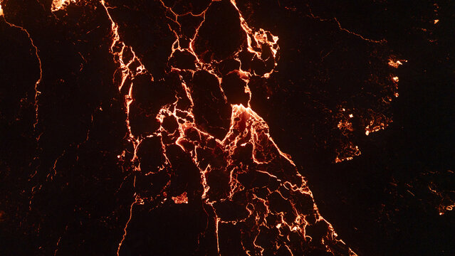 Aerial view of glowing molten lava flowing through dark volcanic rock fissures at night in Reykjavik, Reykjavikurborg, Iceland.
