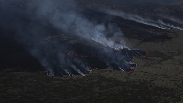 Aerial view of an active volcanic eruption with glowing lava flows and thick smoke plumes rising from the rugged landscape in Reykjavik, Reykjavikurborg, Iceland.