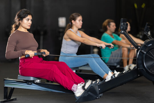 Latina woman in sportswear doing an intense circuit workout on a rowing machine during a Crossfit class in the gym. Woman doing exercises to lose weight