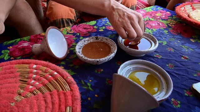 Marrakech, morocco. August 9, 2026. Hand dipping a piece of bread into a bowl of argan oil. Authentic moroccan breakfast with amlou, olive oil, and bread on a colorful table