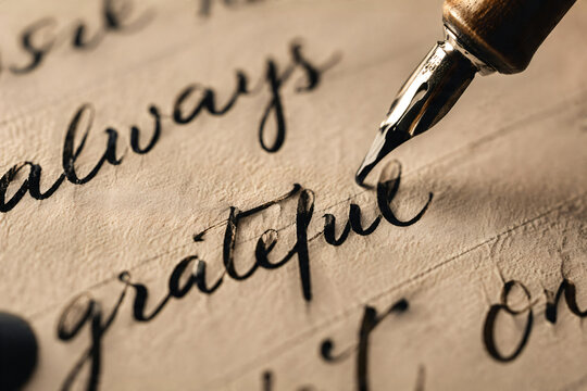 Beautiful vintage closeup macro of elegant fountain pen nib writing cursive always grateful calligraphy text on textured antique paper for gratitude.