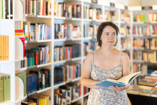 Adult woman stands in bookstore, carefully browsing shelves and selecting book of interest
