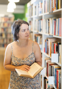 Adult woman stands in bookstore, carefully browsing shelves and selecting book of interest