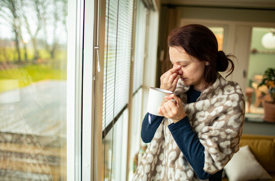 Woman with sinus headache holding tea by window at home