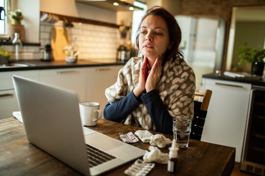 Woman holding throat on video call at home kitchen