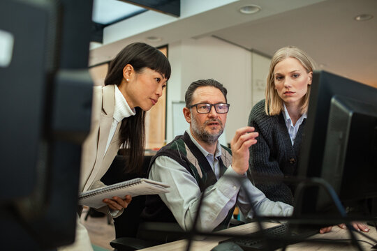 Three coworkers collaborating at computer in modern office