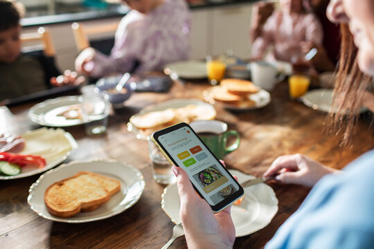 Parent using smartphone app at family breakfast table at home