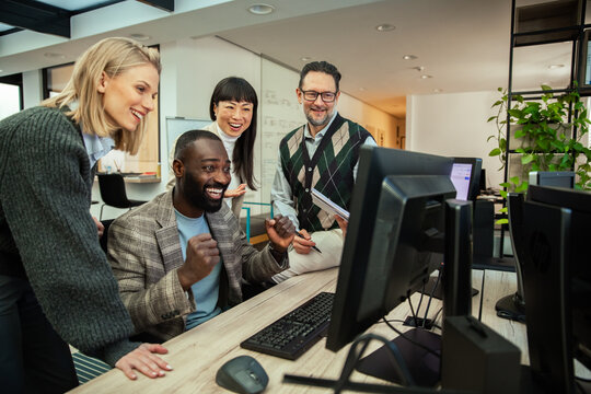 Happy coworkers celebrating success at computer in modern office