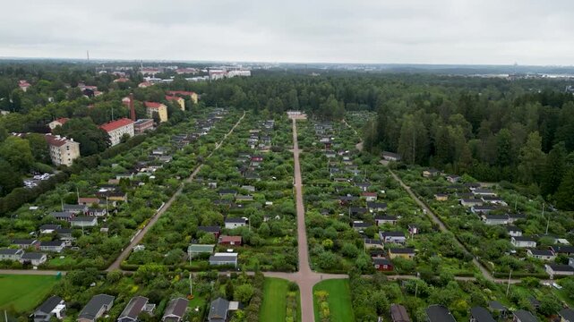 aerial drone video of Kumpula Allotment Gardens in Helsinki, Finland, surrounded by lush green vegetation, garden plots, small cottages, and peaceful summer scenery.