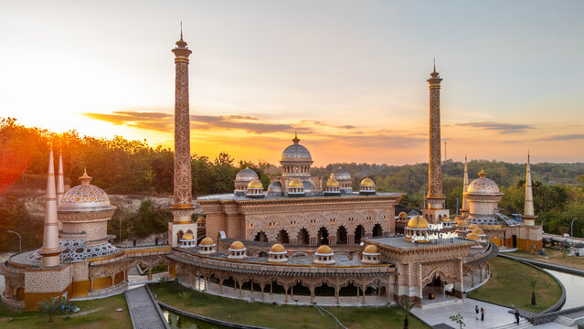 Aerial view of Samin Baitul Muttaqin Mosque with its golden domes and tall minarets illuminated by the warm glow of sunset in Bojonegoro, East Java, Indonesia.