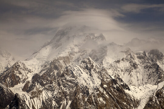 Aerial view of Broad Peak covered in snow and ice with a lenticular cloud formation over the summit and rugged mountain ridges, Skardu, Pakistan.