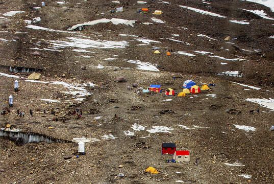 Aerial view of the Concordia camping site along the K2 trek in the Karakorum range, featuring colorful tents scattered across rocky glacial terrain with patches of snow in Skardu, Pakistan.