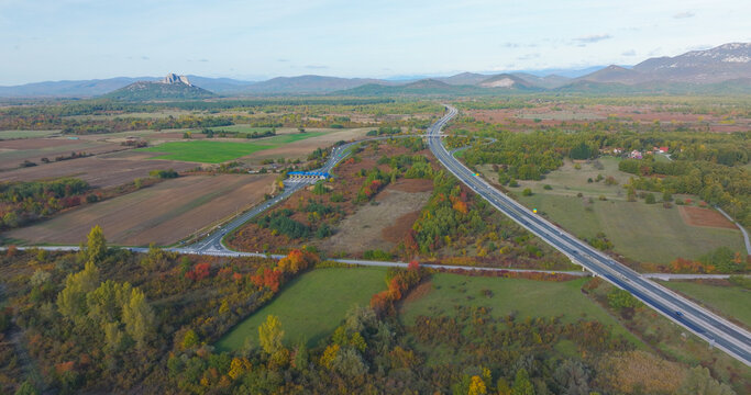 AERIAL: Motorway interchange surrounded by colourful autumn landscape in Croatia. Roads, fields, scattered woodland and distant hills merge into a scenic blend of nature and modern infrastructure.