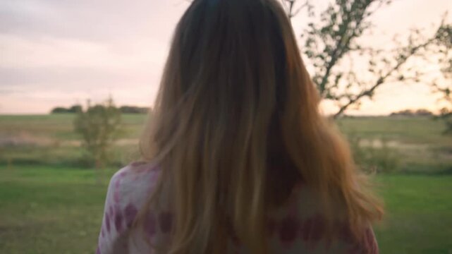 Woman walking through garden toward open fields at sunset