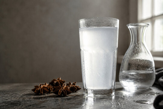 Glass of milky anise liquor with star anise and water carafe on dark stone, traditional liqueur tasting concept