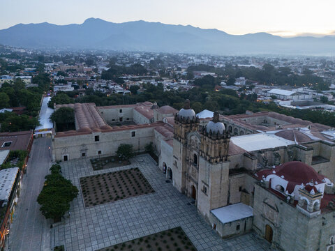 Aerial view of the historic Santo Domingo de Guzman church with its stone facade and red domes, surrounded by the urban landscape of Oaxaca, Oaxaca, Mexico.