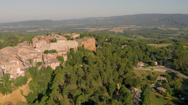 Aerial drone view of the hilltop French village of Roussillon surrounded by famous ochre cliffs at sunrise, Provence