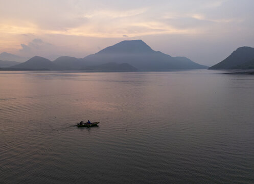 Aerial view of a small boat with people on a calm lake during sunrise, surrounded by misty mountains in Jalapa, Oaxaca, Mexico.