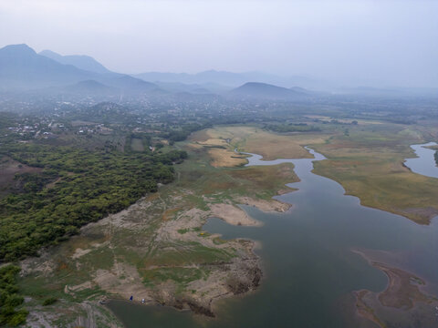 Aerial view of the reservoir and surrounding landscape with lush green vegetation, dry fields, and distant mountains in Jalapa del Marques, Oaxaca, Mexico.
