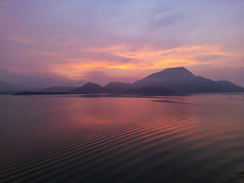 Aerial view of sunrise over a calm lake with gentle ripples and distant mountains under a vibrant purple and orange sky in Jalapa, Oaxaca, Mexico.