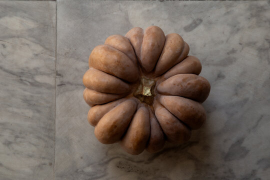 Whole pumpkin placed on a white and grey marble floor.