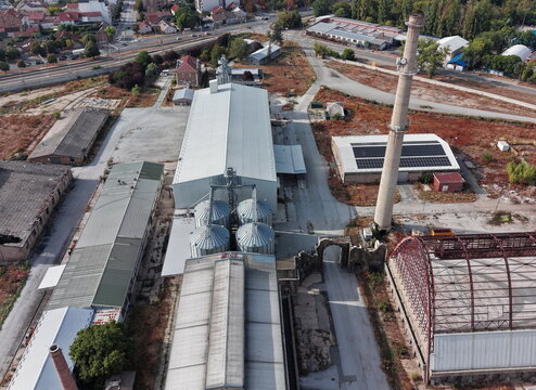 Aerial view of the historic glass factory featuring industrial buildings, metal silos, and a tall chimney surrounded by urban infrastructure in Pancevo, Vojvodina, Serbia.