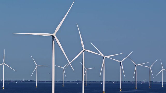 Rows of offshore wind turbines rise from open water at Windpark Fryslan near Breezanddijk Netherlands under a clear blue sky