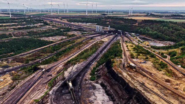 Aerial view shows the Garzweiler open-pit coal mine with conveyor tracks, excavation pits and rows of wind turbines on the horizon in Germany