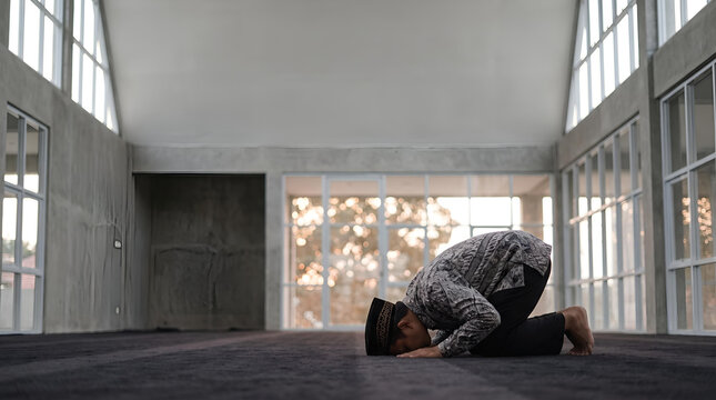 Muslim man praying in sujood position in a modern mosque with large windows and natural light, peaceful contemplation