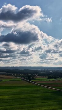 Wide view of countryside near Schwedt, Germany, with green agricultural fields, a winding road and dramatic clouds casting shifting light across the open landscape.