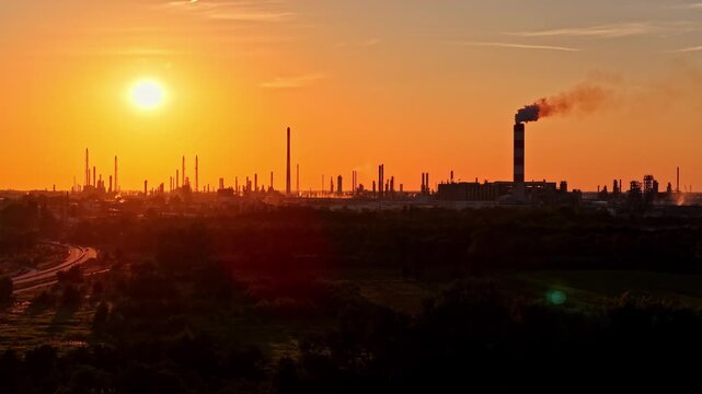 PKN Orlen Płock Production Plant smokestack releases smoke over a wide refinery complex at vivid orange sunset.