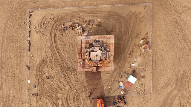 Aerial view of the Vreugdevuur Scheveningen bonfire structure constructed from wooden pallets on the sandy beach, surrounded by tire tracks and fencing in Den Haag, Zuid-Holland, Netherlands.