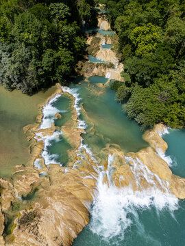 Aerial view of the turquoise cascades and terraced limestone pools of the Agua Azul waterfalls surrounded by lush tropical jungle vegetation in Agua Azul, Chiapas, Mexico.